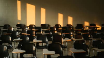 Leerer Seminarraum mit Reihen leerer Stühle, warmes Licht fällt durch die Fenster