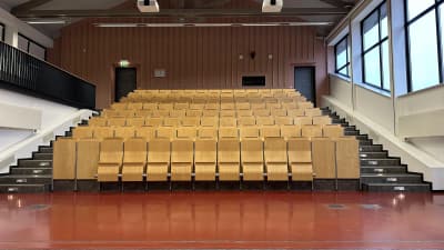 Leerer Hörsaal mit ansteigenden Reihen heller Holzklappsitze vor Semesterbeginn