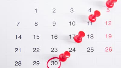 Kalender mit roten Pinnnadeln und einem rot umkreisten Datum als Symbol für eine nahende Frist